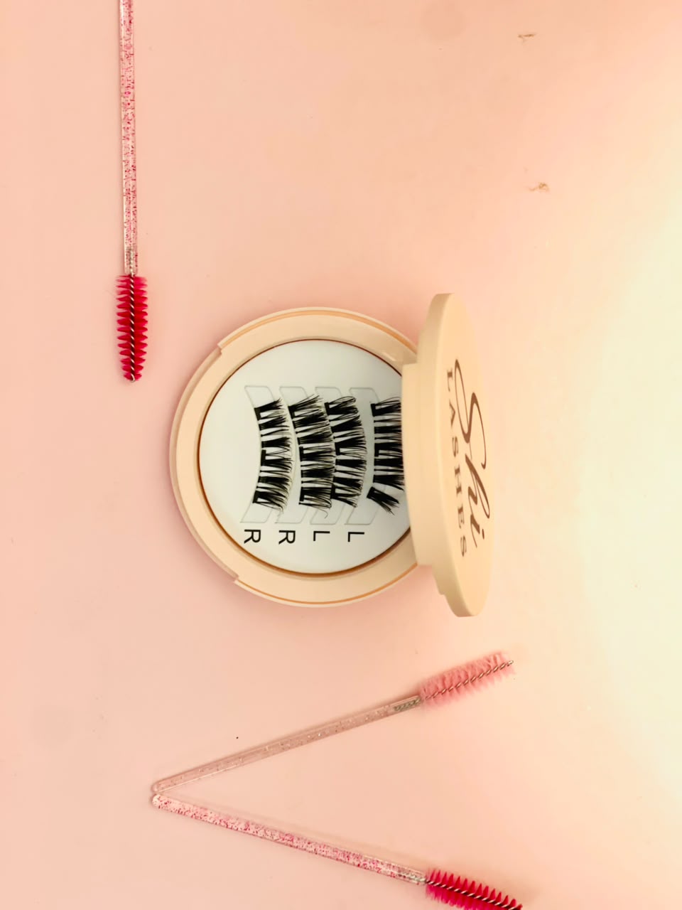 Shi Lashes open compact with magnetic lashes and pink spoolie brushes on soft pink background