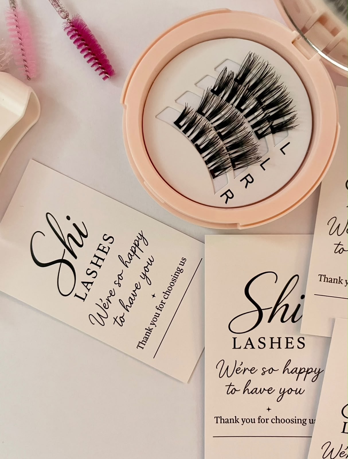 Shi Lashes kit flat lay with thank you cards, spoolie brushes, and lash applicator on pink surface